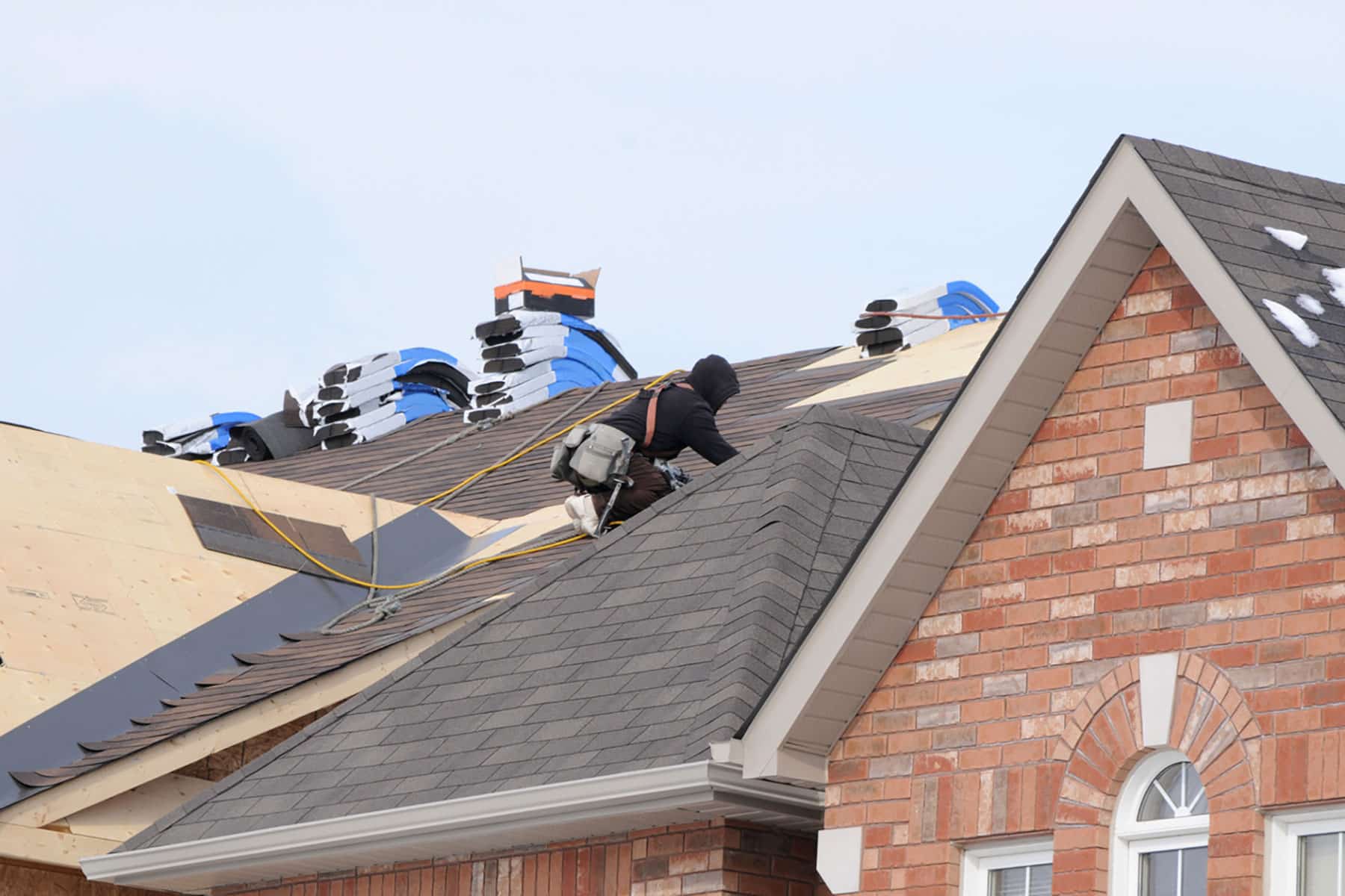 Skilled Craftsmanship: Our team of experienced professionals is dedicated to delivering exceptional workmanship, ensuring that every expert roof replacement in Midland, TX, meets our high standards of quality and safety., Roofers laying new shingles beside a brick gable during residential roofing in West Odessa - TX